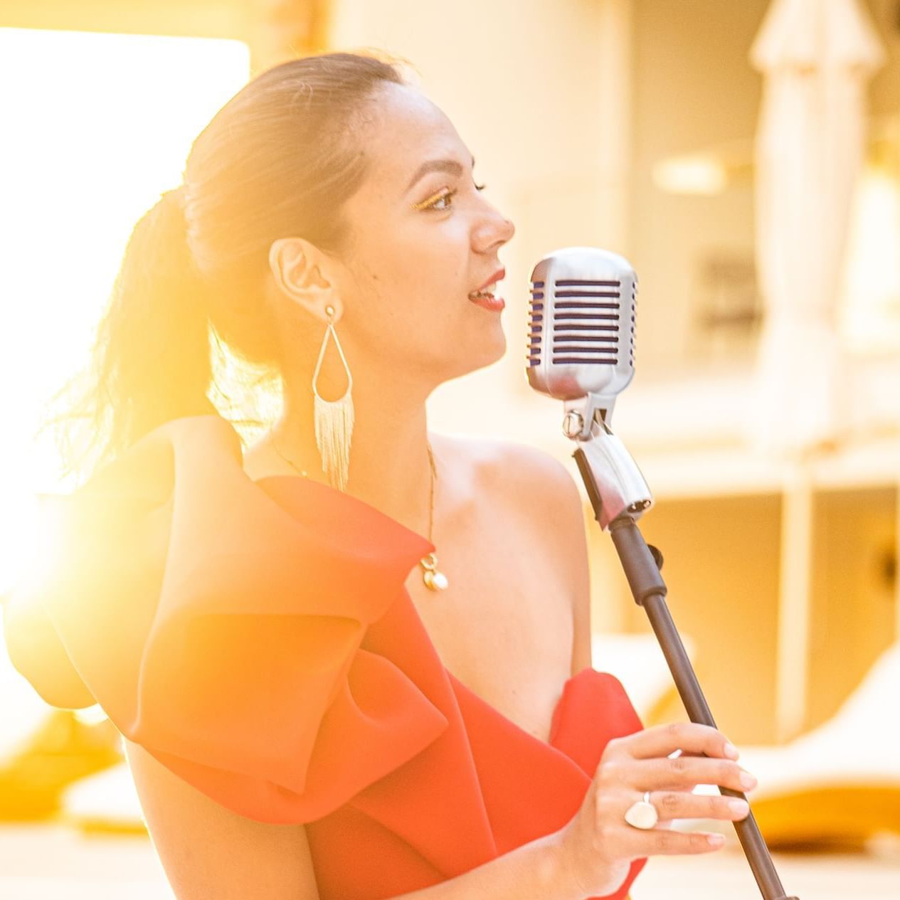 Woman in an orange dress singing into a vintage microphone on a sunlit terrace at The Morgan Resort Spa Village