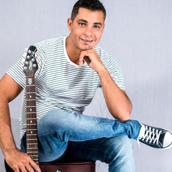 Musician in striped shirt posing by a guitar headstock, performing live at The Morgan Resort Spa Village
