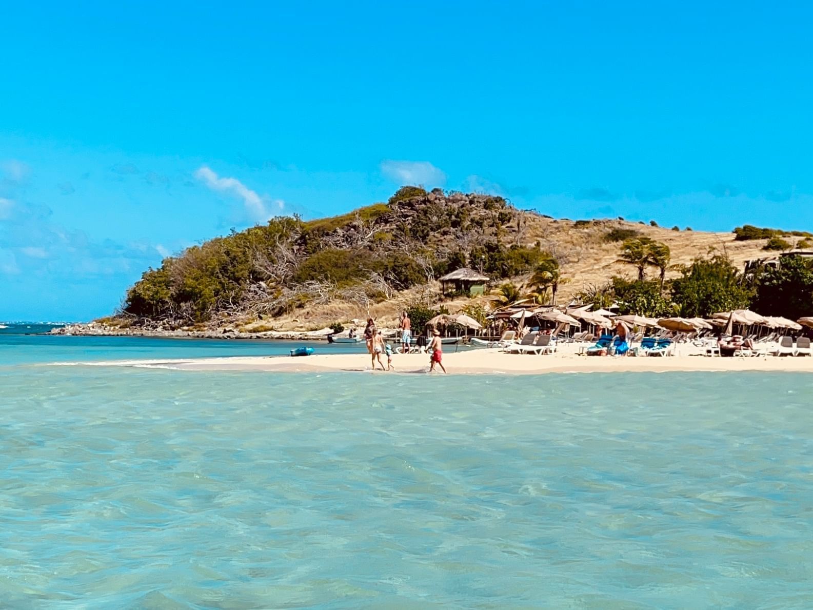 Landscape view of Pinel Island with thatched umbrellas by the shore & scrubby hills near Morgan Resort Spa Village