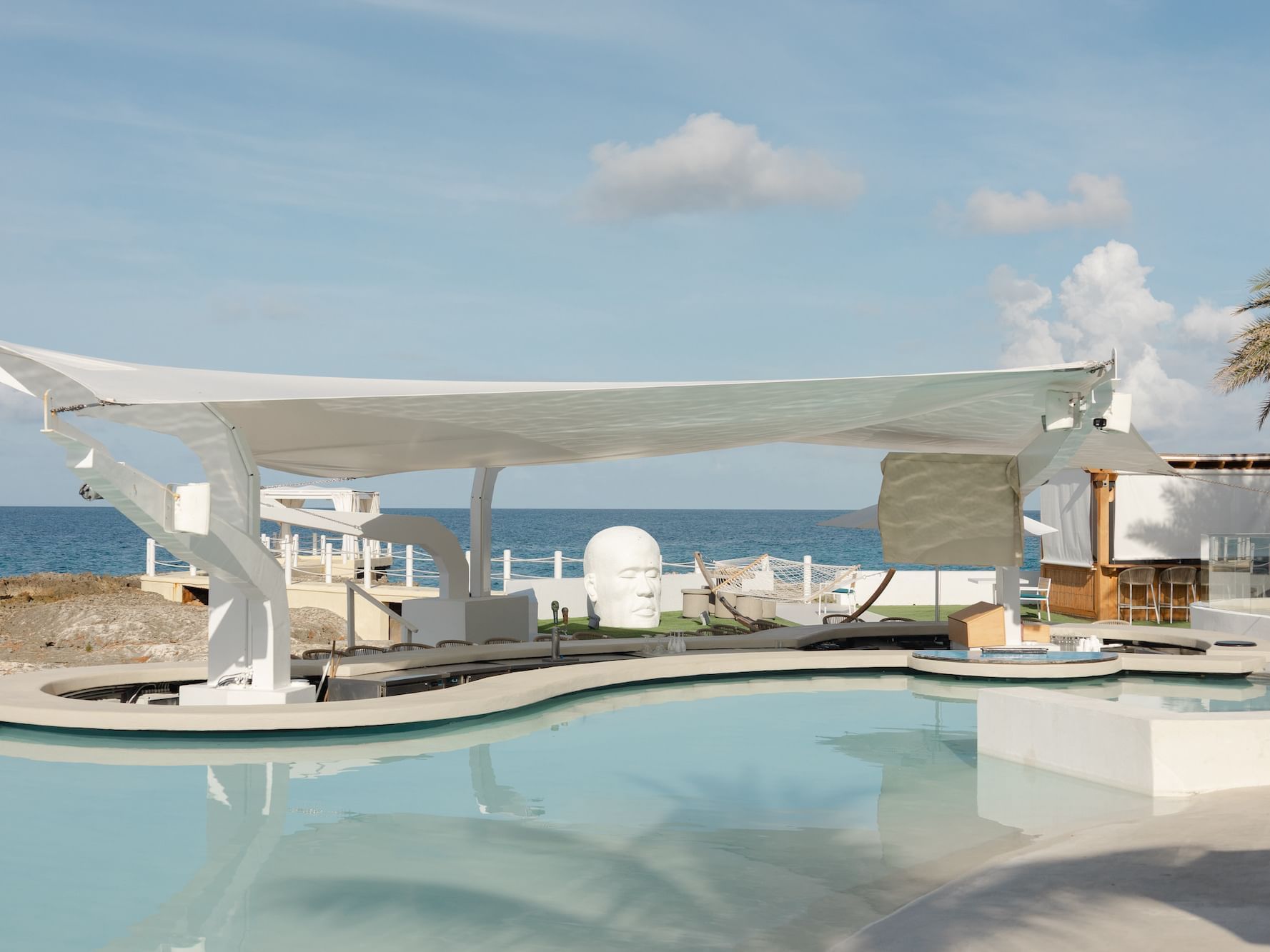 Bar-M pool bar featuring a white head sculpture placed by the pool under a tension canopy at The Morgan Resort Spa Village
