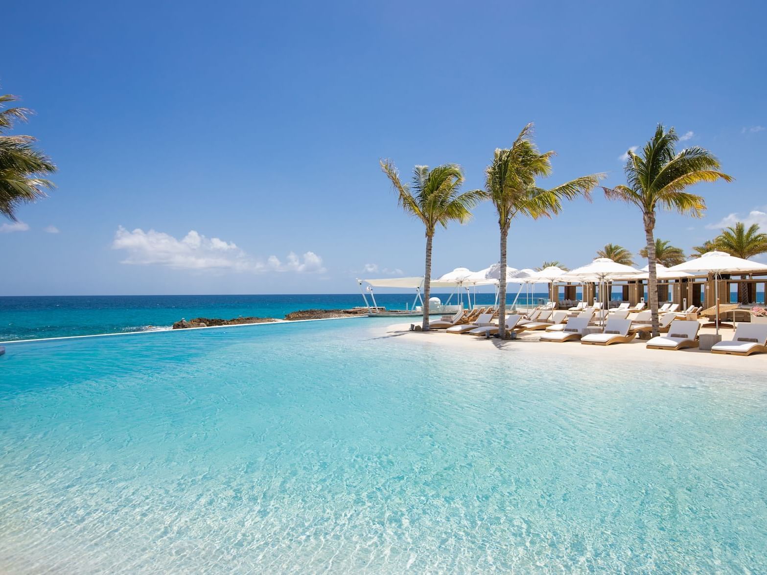 Infinity pool with white loungers and palm trees by the ocean at The Morgan Resort Spa Village