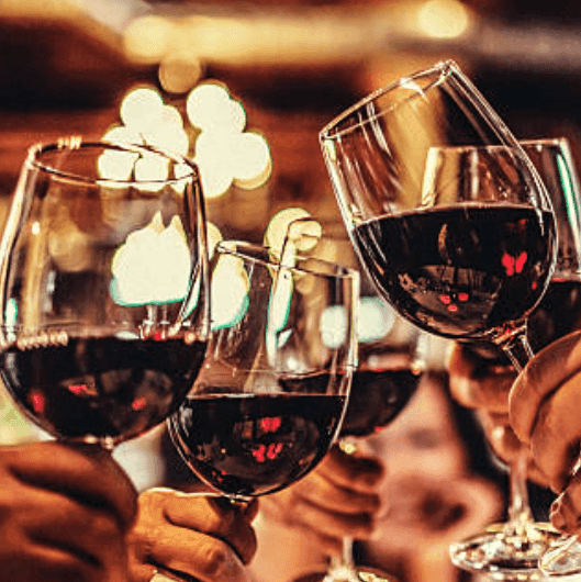Four people clinking red wine glasses in a cozy, warmly lit bar during Wind Down Mondays at The Morgan Resort Spa Village